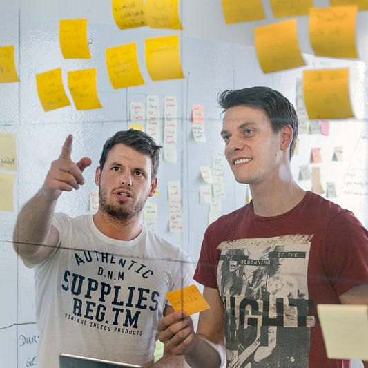 Two men in front of transparent screen with post-it notes